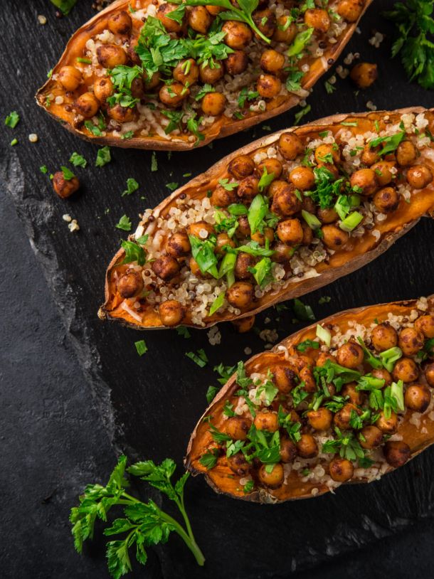 Roasted sweet potato halves stuffed with quinoa, chickpeas, and chopped parsley on a dark slate surface with lime wedges nearby.