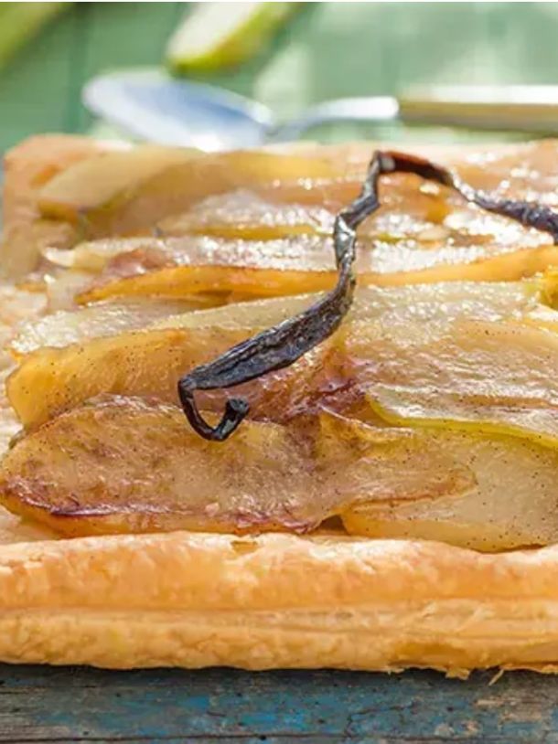 Square pear tart with caramelized pear slices and a vanilla bean on a rustic wooden table, glossy pastry edge intact.