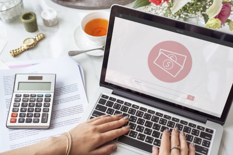 Un ordinateur portable avec un écran affichant des icônes de billets, un calculateur, une tasse de thé et des notes sur une table.