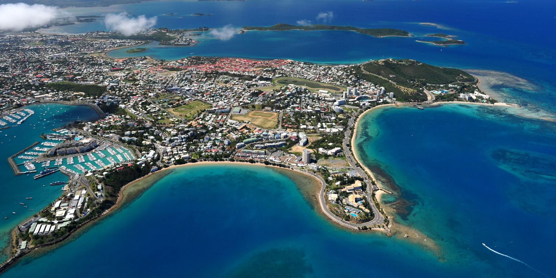 Aerial view of a coastal town with a large marina, turquoise bays, and sandy beaches surrounding a densely built shoreline.