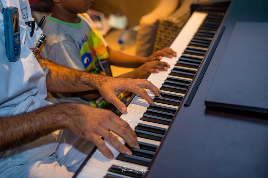 Adult and child playing piano together, hands on the keys in a warm room, suggesting music time or therapy session.