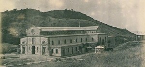 Historic two-story stone building with arched windows on a hillside, in a rural setting.