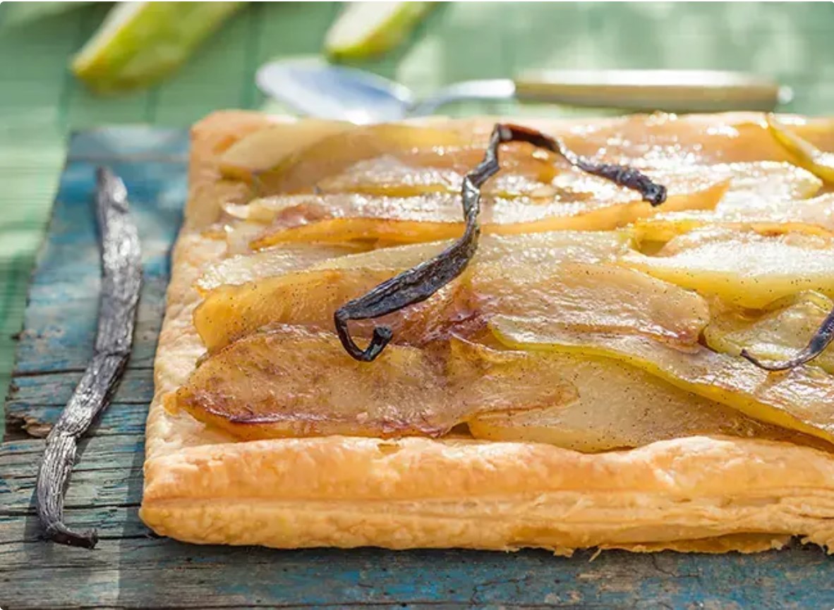 Square pear tart with caramelized pear slices and a vanilla bean on a rustic wooden table, glossy pastry edge intact.