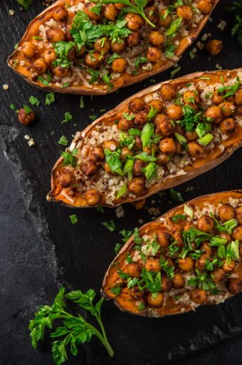 Roasted sweet potato halves stuffed with quinoa, chickpeas, and chopped parsley on a dark slate surface with lime wedges nearby.
