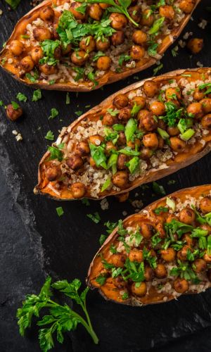 Roasted sweet potato halves stuffed with quinoa, chickpeas, and chopped parsley on a dark slate surface with lime wedges nearby.