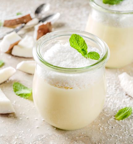 Vegan sweet food coconut panna cotta dessert in glass jar with coconut chips and mint leaves light concrete stone background copy space