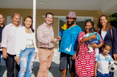 Diverse group of adults with a baby and a child posing for a photo outside a beige house porch.