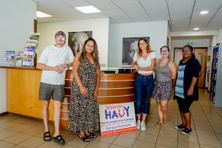 Group of five adults posing in a bright lobby near a curved wooden reception desk, with a 'Valentin Hauy' sign in front (charity event).