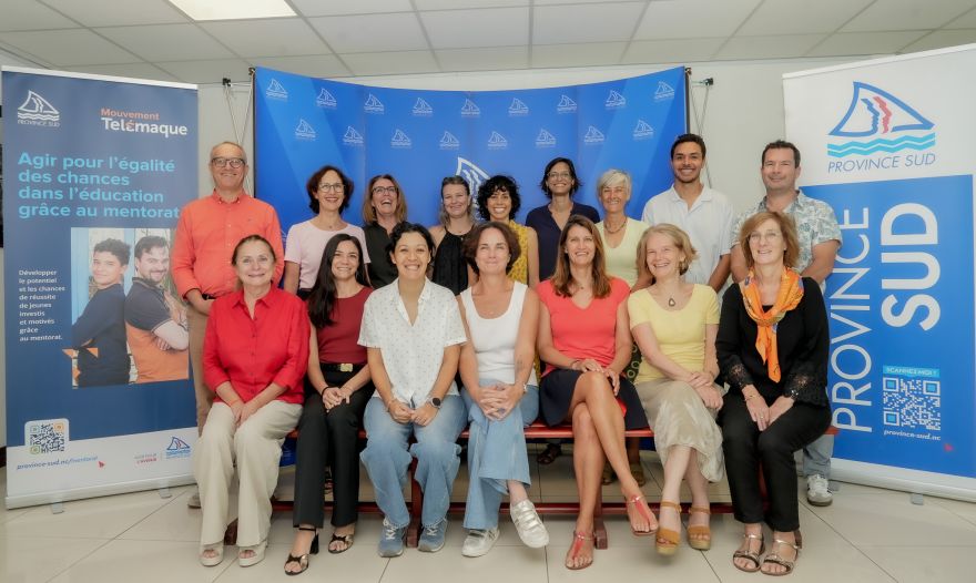 Group of adults smiling for a photo in front of blue event banners and a Province Sud backdrop, indoors on a red bench formation behind them.