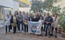 Group of diverse people posing outdoors on a wooden deck, holding a banner that says 'Ambassadeur du lagon' and smiling at the camera.