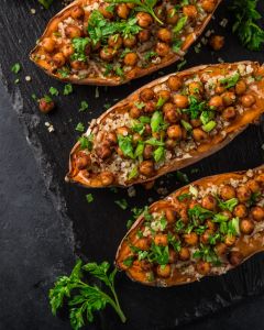 Roasted sweet potato halves stuffed with quinoa, chickpeas, and chopped parsley on a dark slate surface with lime wedges nearby.