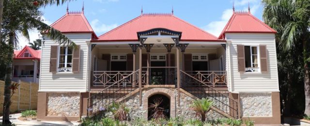 Two-story house with light siding, red roof, stone foundation, front porch and decorative iron railings on both sides.