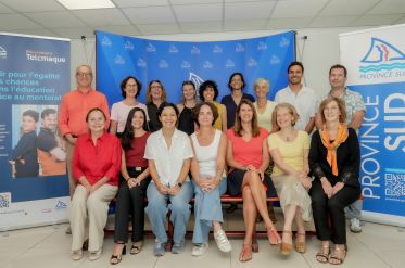 Group of adults smiling for a photo in front of blue event banners and a Province Sud backdrop, indoors on a red bench formation behind them.