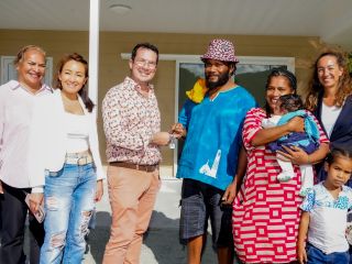 Diverse group of adults with a baby and a child posing for a photo outside a beige house porch.