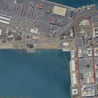 logo : Aerial view of a harbor with a container yard, colorful shipping containers, cranes, and docked ships along the water edge.