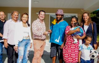 Diverse group of adults with a baby and a child posing for a photo outside a beige house porch.