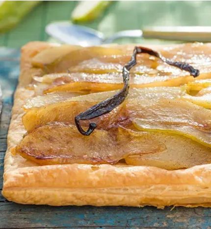 Square pear tart with caramelized pear slices and a vanilla bean on a rustic wooden table, glossy pastry edge intact.