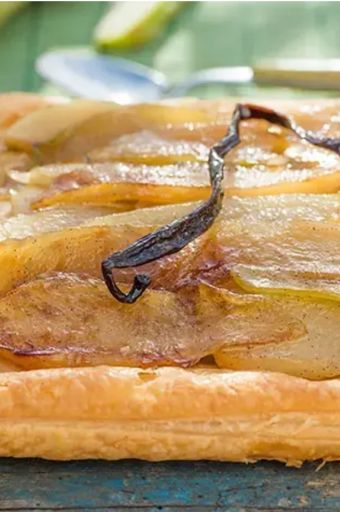Square pear tart with caramelized pear slices and a vanilla bean on a rustic wooden table, glossy pastry edge intact.