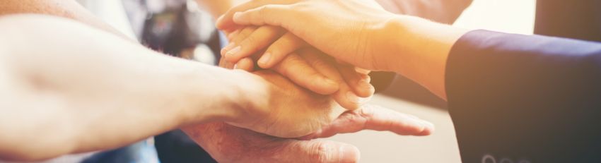 Hands stacked together in a circle, symbolizing teamwork and unity in a sunlit room