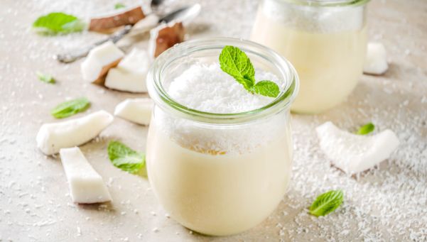 Vegan sweet food coconut panna cotta dessert in glass jar with coconut chips and mint leaves light concrete stone background copy space