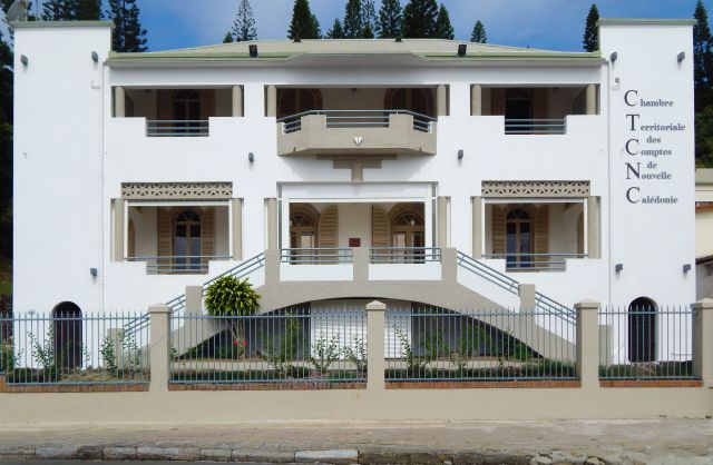 White multi‑story building with balconies and a tall vertical sign on the right reading 'Chambre Territoriale des Comptes de Nouvelle Calédonie'.