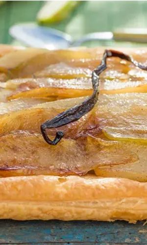 Square pear tart with caramelized pear slices and a vanilla bean on a rustic wooden table, glossy pastry edge intact.