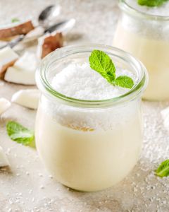Vegan sweet food coconut panna cotta dessert in glass jar with coconut chips and mint leaves light concrete stone background copy space