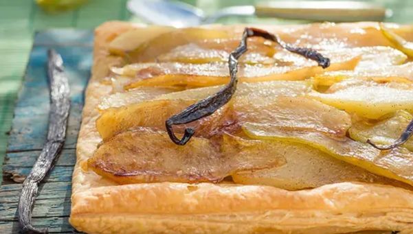Square pear tart with caramelized pear slices and a vanilla bean on a rustic wooden table, glossy pastry edge intact.