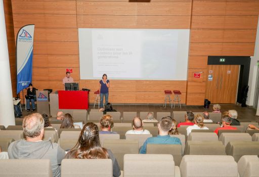 Speaker at a red lectern presenting to an audience in a conference hall, with a large projected slide on a wood-paneled wall behind them.