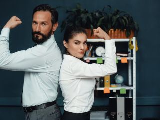 Two professionals strike a confident back-to-back pose in an office setting.