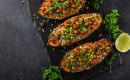 Roasted sweet potato halves stuffed with quinoa, chickpeas, and chopped parsley on a dark slate surface with lime wedges nearby.
