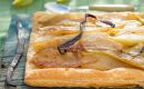 Square pear tart with caramelized pear slices and a vanilla bean on a rustic wooden table, glossy pastry edge intact.
