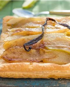 Square pear tart with caramelized pear slices and a vanilla bean on a rustic wooden table, glossy pastry edge intact.