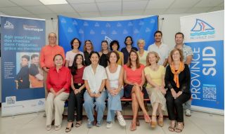 Group of adults smiling for a photo in front of blue event banners and a Province Sud backdrop, indoors on a red bench formation behind them.