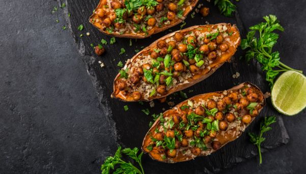 Roasted sweet potato halves stuffed with quinoa, chickpeas, and chopped parsley on a dark slate surface with lime wedges nearby.